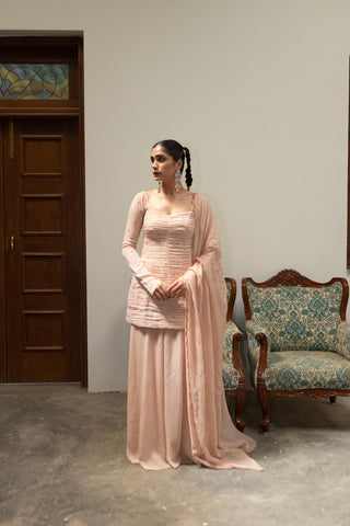 Complete light baby pink ruching peplum set with embroidered scallop dupatta and sharara styled for festive and wedding occasions.