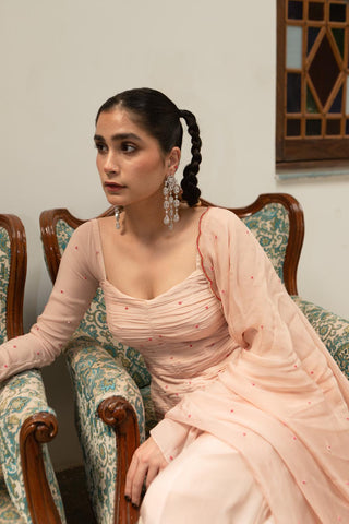 Designer baby pink ruching peplum set featuring moti chitta detailing, fitted silhouette, and embroidered scallop dupatta with sharara. Designed by Ease.