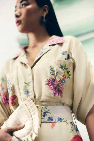 Minimal ivory jumpsuit showcasing delicate embroidered pockets and a tie-up belt for shape. A graceful and stylish option for daytime events, blending elegance with ease.