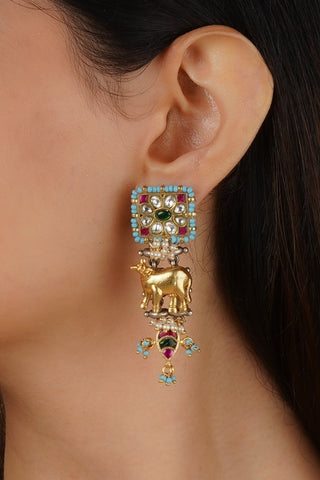 Close-up of a person wearing a decorative earring with a cow figure and gemstones. A perfect artificial imitation jewellery for pairing with cocktail or boho dresses.
