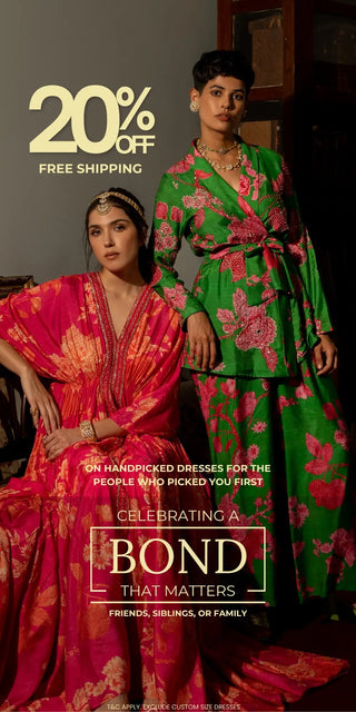 Two women modeling traditional Indian floral printed kurta sets in a dark indoor setting. One kurta is bright pink with gold embroidery, and the other is green co-ord set with pink floral print.