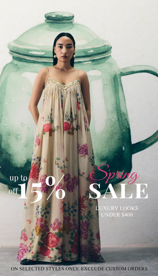 A woman wearing a cream floral Jumpuit stands to pose with promotional text on the left reading 'Spring SALE' and 'up to 15% off'. Luxury Looks Under $400. shop New In Edit.
