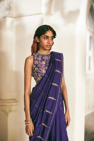 A women in a solid purple saree adorned with exquisite hand-embroidered lines and delicate floral accents. Perfect for destination wedding, festive occasions and special hosting parties