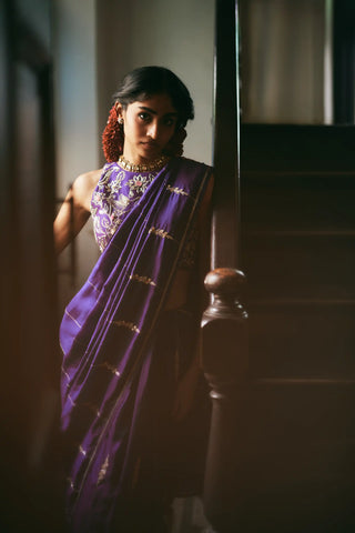 A women in a solid purple saree adorned with exquisite hand-embroidered lines and delicate floral accents. Perfect for destination wedding, festive occasions and special hosting parties