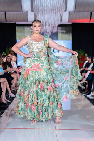 A rich green and ivory floral printed pre-draped chiffon ruffle saree featuring elegant prints and tiered lace detailing that adds a fluid movement. It is paired beautifully hand-embroidered blouse. Designed by Paulmi and Harsh.