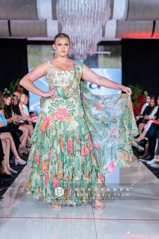 A rich green and ivory floral printed pre-draped chiffon ruffle saree featuring elegant prints and tiered lace detailing that adds a fluid movement. It is paired beautifully hand-embroidered blouse. Designed by Paulmi and Harsh.