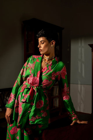 A woman wearing a green and pink floral printed blazer style with metallic embellishments, posed in a dimly lit interior setting.