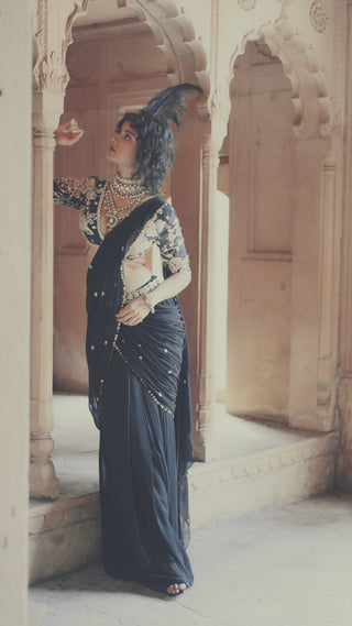 Model in black pre-stitched cocktail saree, hand-embroidered in delicate floral motifs and lace detailing in V-neck deep blouse, posing for photoshoot. The pallu features metal sequin work and floral buttis designed by Paulmi and Harsh.
