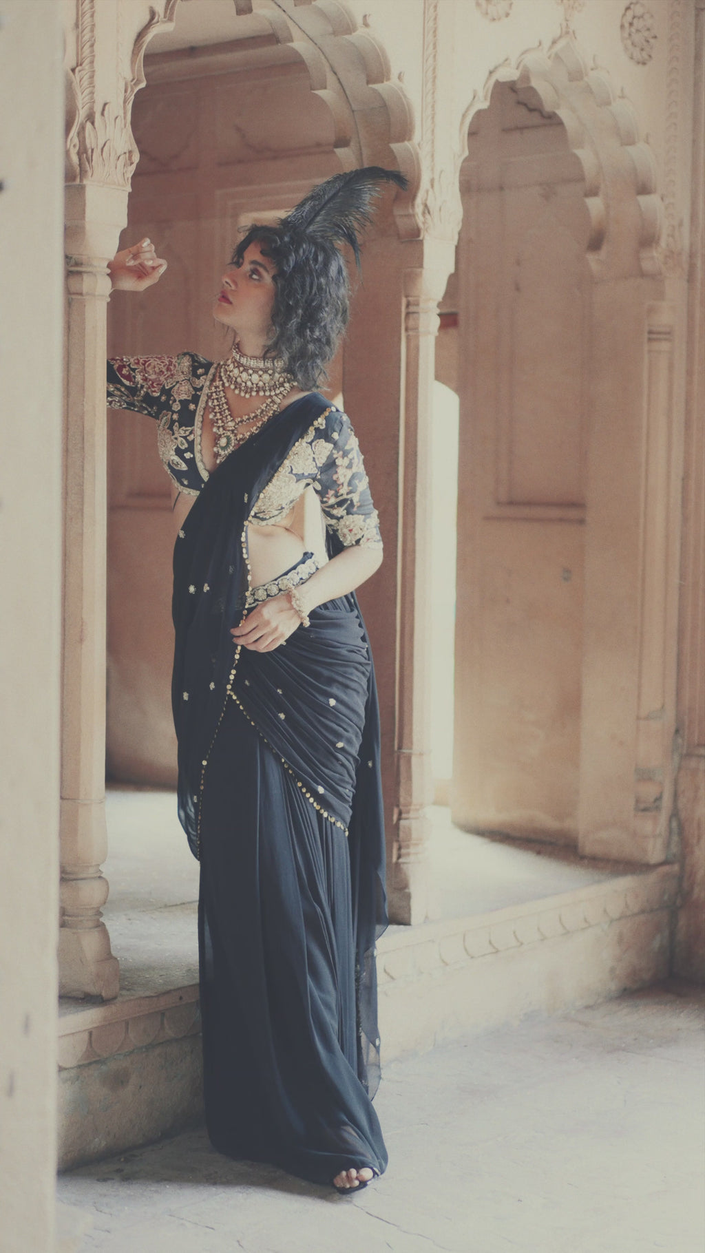 Model in black pre-stitched cocktail saree, hand-embroidered in delicate floral motifs and lace detailing in V-neck deep blouse, posing for photoshoot. The pallu features metal sequin work and floral buttis designed by Paulmi and Harsh.