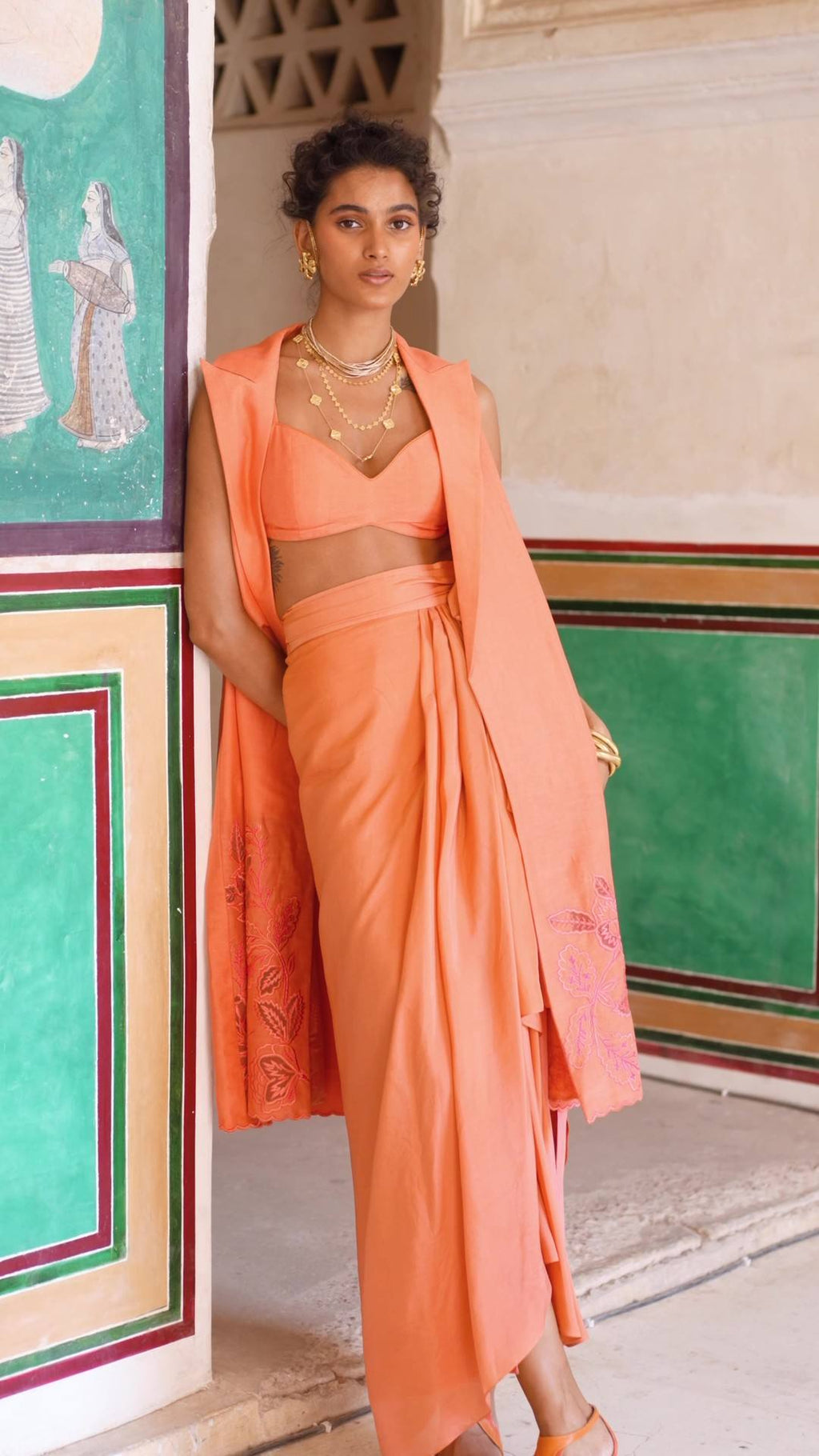 A chic coral jacket and blouse crafted from linen paired with a silk organza skirt. The jacket is designed with cutwork detailing using our floral motifs.      Elevate the dress with gold accessories, skirt comes with pre–stitched wrap detailing and is fully lined. Perfect outfit for resort, vacations, brunches, evening gala, parties. Designed by Paulmi and Harsh.