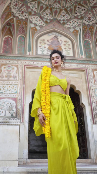 Model wearing Lime Yellow crop Top, Cape, draped skirt and bralette top - Choga Set designed by Paulmi and Harsh. A perfect women clothing for Indian traditional ceremonies, formal events, Festivities, weddings, engagement, evening functions, special occasions, formal work events, evening parties etc.