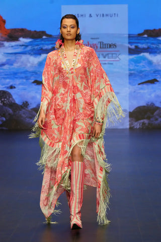 A model walks the runway wearing a coral pink and beige patterned kaftan with white fringe, paired with pink and white striped thigh-high boots. Gale Kaftan by Rishi and Vibhuti features a refined mint and dusty rose palette with hand embroidery and trims on a crepe one-piece ensemble.