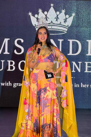 Model holding mike during fashion runway showcasing organza crepe yellow floral lehenga set with handcrafted embellishments, and vibrant contemporary styling.