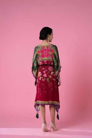 Back view of a red and green floral printed kaftan with an evenly blended gradient effect, showcasing the full fall of the fabric and pom-pom lace detailing around the hem.