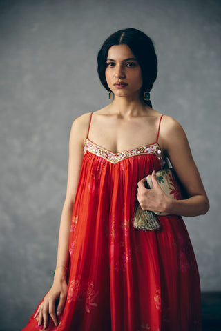 Woman in a statement red floral chic jumpsuit holding a clutch all set ready to go to a launch party. 